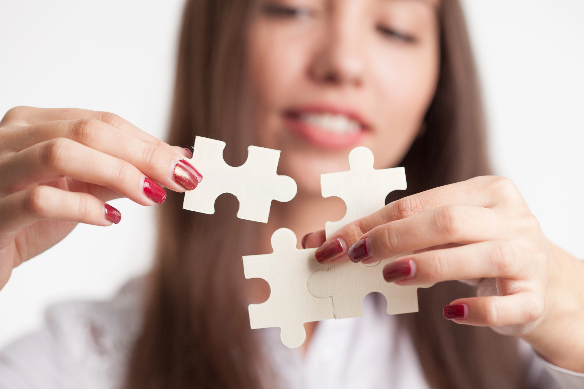 Alt text: "Een jonge vrouw met rood gelakte nagels houdt twee witte puzzelstukjes vast die ze op het punt staat in elkaar te passen.