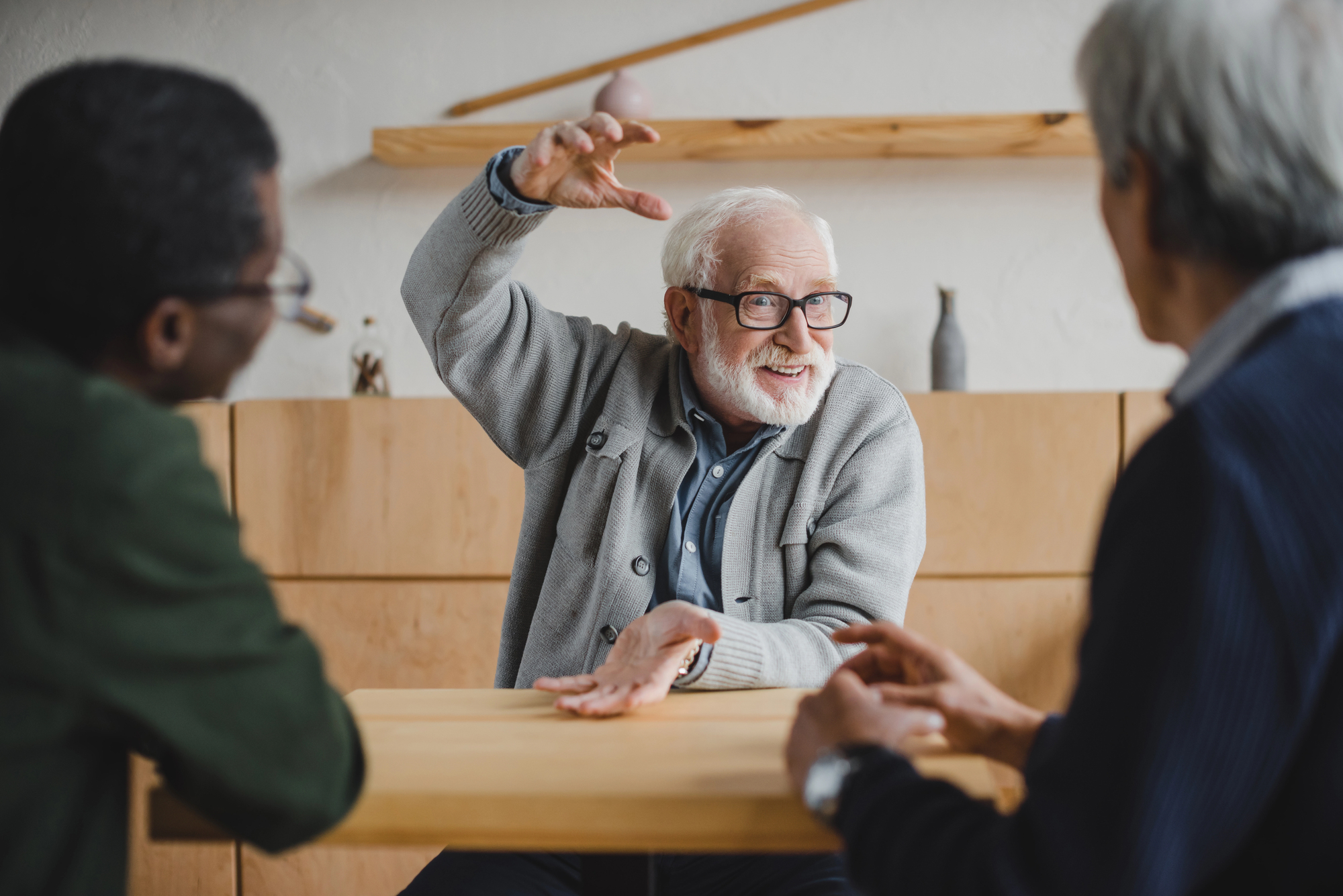 storybrand versus golden circle Oudere man met grijze baard en bril gebaard enthousiast tijdens gesprek met twee mensen aan houten tafel